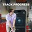 Man in a garage looking at a smartphone displaying app progress with text 'Track Progress'.