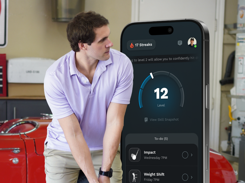 Man in a garage is looking at a smartphone displaying an app with a progress bar on the screen.